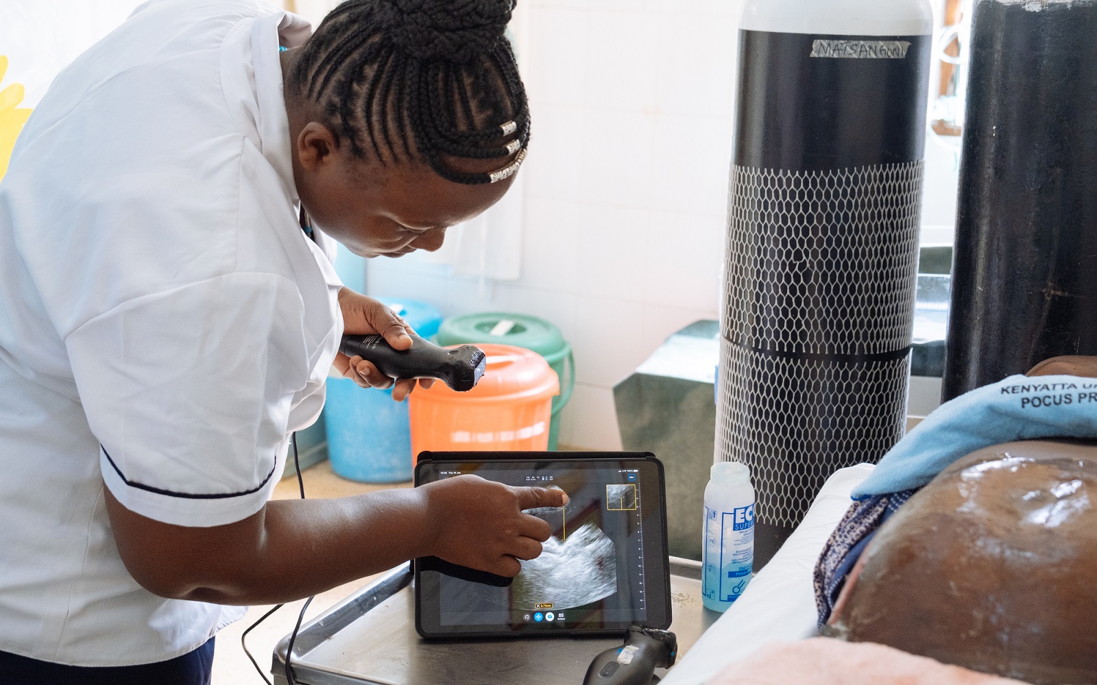 A clinician uses a handheld ultrasound and tablet during a prenatal checkup